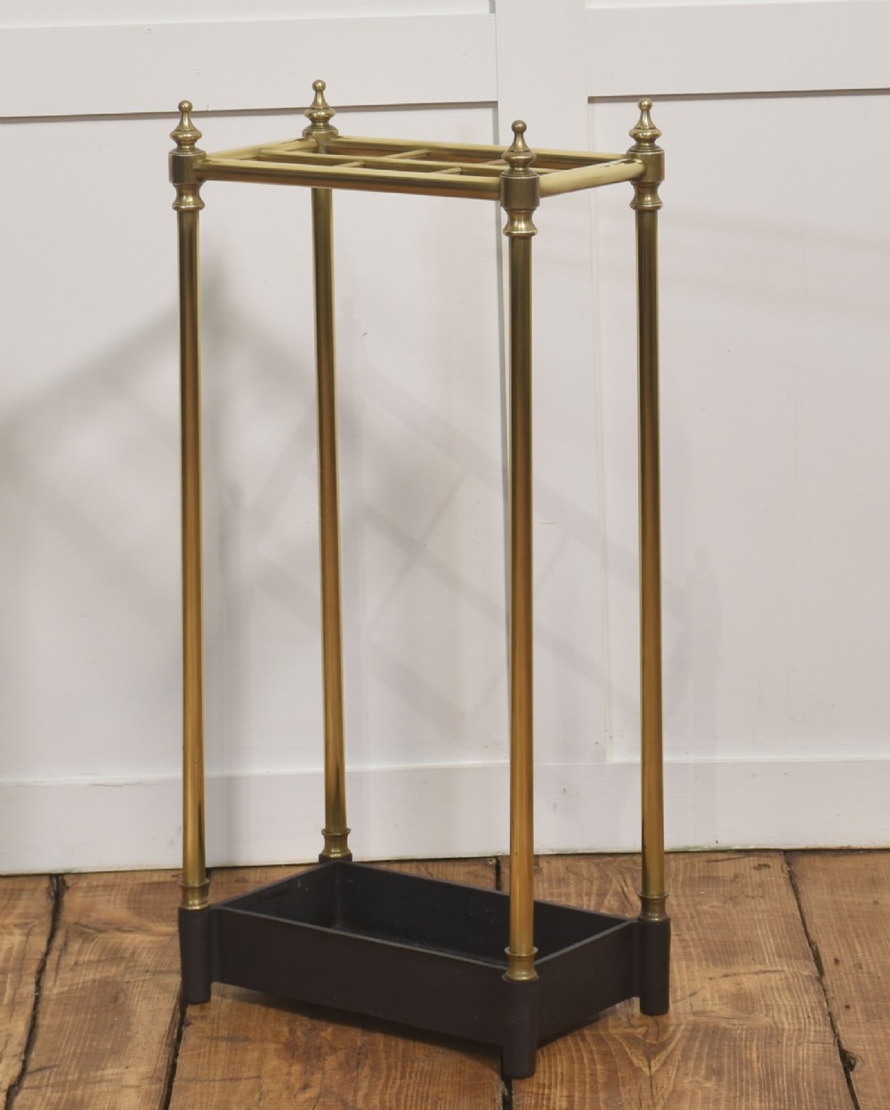 A 19th-century rectangular umbrella stand featuring brass upright posts, brass top rail dividers with corner finials, and a dark cast iron drip tray base.