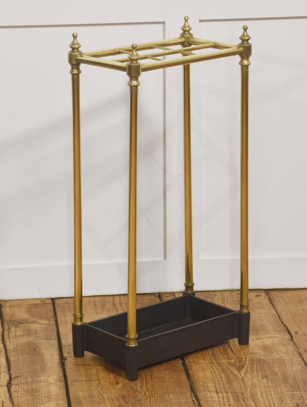 A 19th-century rectangular umbrella stand featuring brass upright posts, brass top rail dividers with corner finials, and a dark cast iron drip tray base. View VI