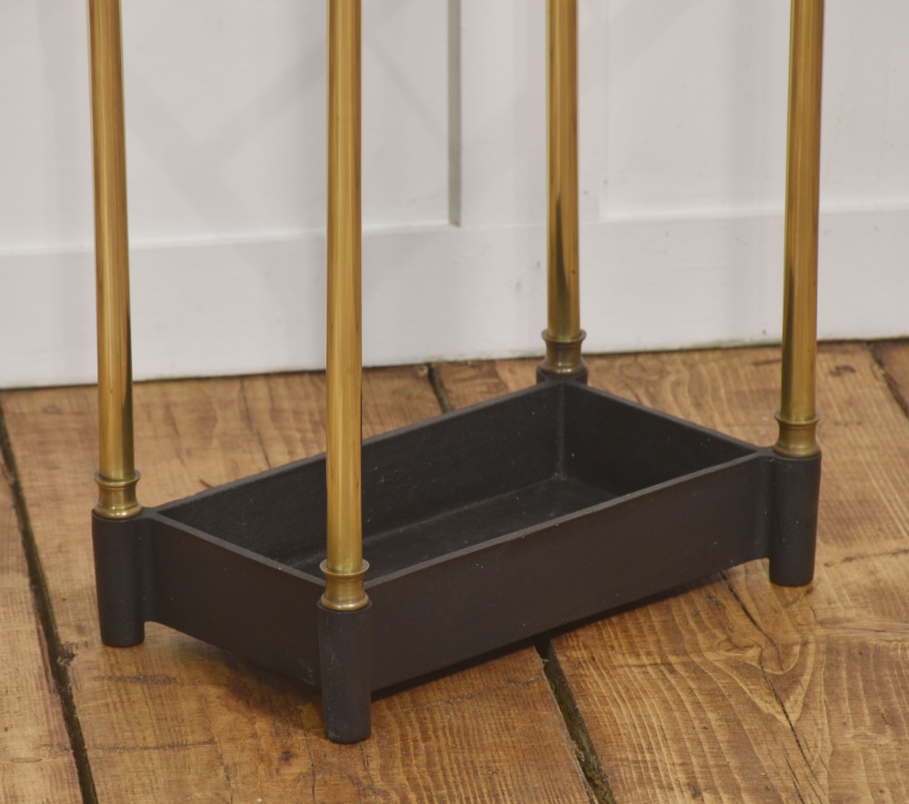 A 19th-century rectangular umbrella stand featuring brass upright posts, brass top rail dividers with corner finials, and a dark cast iron drip tray base. View VII