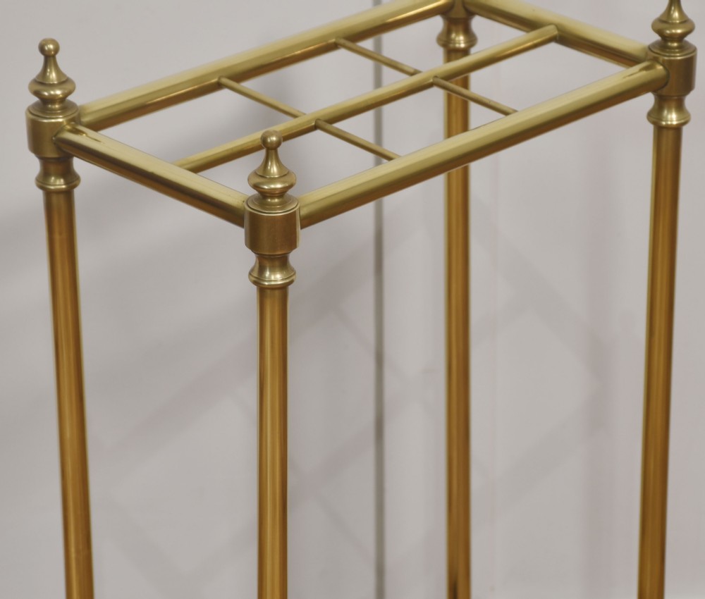 A 19th-century rectangular umbrella stand featuring brass upright posts, brass top rail dividers with corner finials, and a dark cast iron drip tray base. View VIII