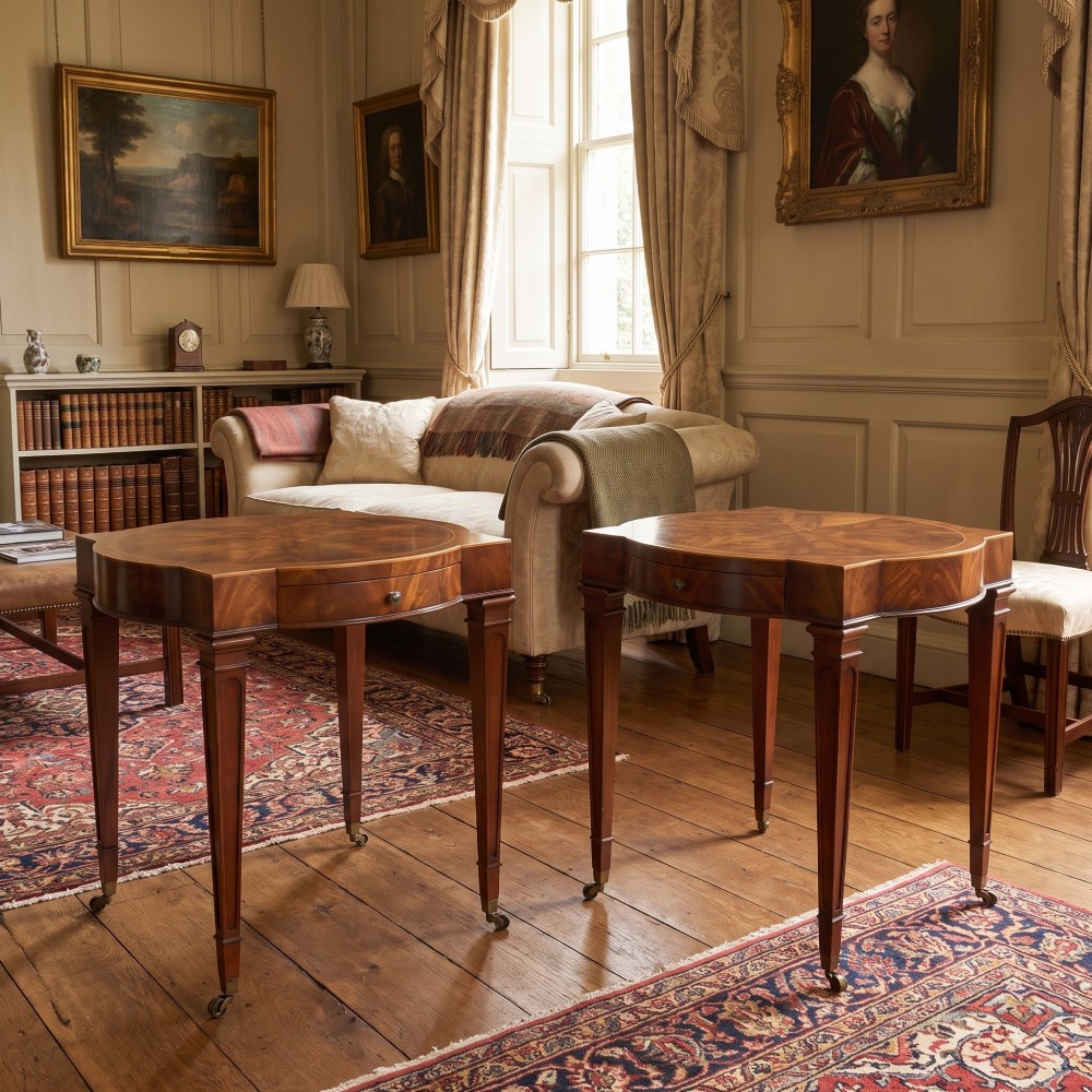A pair of mahogany Sheraton Revival side tables featuring shaped inlaid tops, single frieze drawers, fluted tapered legs, and brass castors. View II