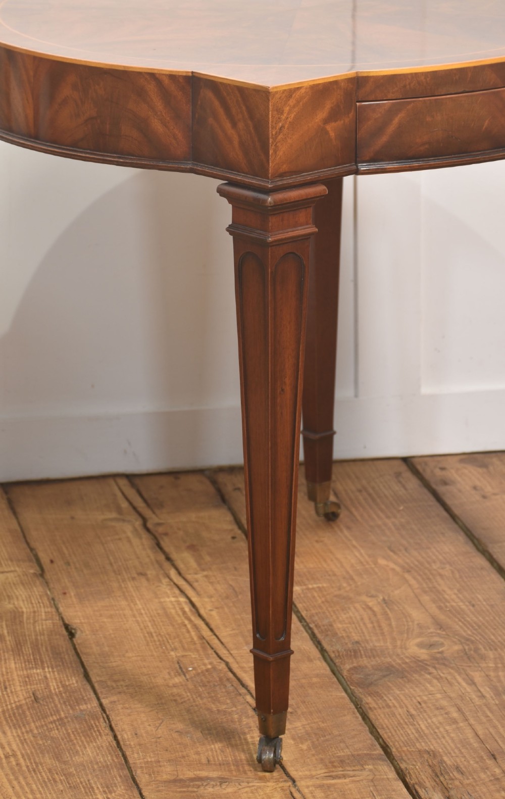 A pair of mahogany Sheraton Revival side tables featuring shaped inlaid tops, single frieze drawers, fluted tapered legs, and brass castors. View IV
