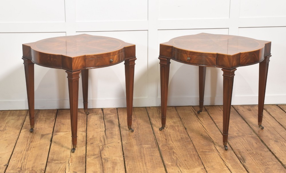 A pair of mahogany Sheraton Revival side tables featuring shaped inlaid tops, single frieze drawers, fluted tapered legs, and brass castors. View IX