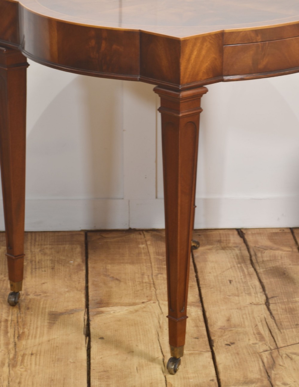 A pair of mahogany Sheraton Revival side tables featuring shaped inlaid tops, single frieze drawers, fluted tapered legs, and brass castors. View X