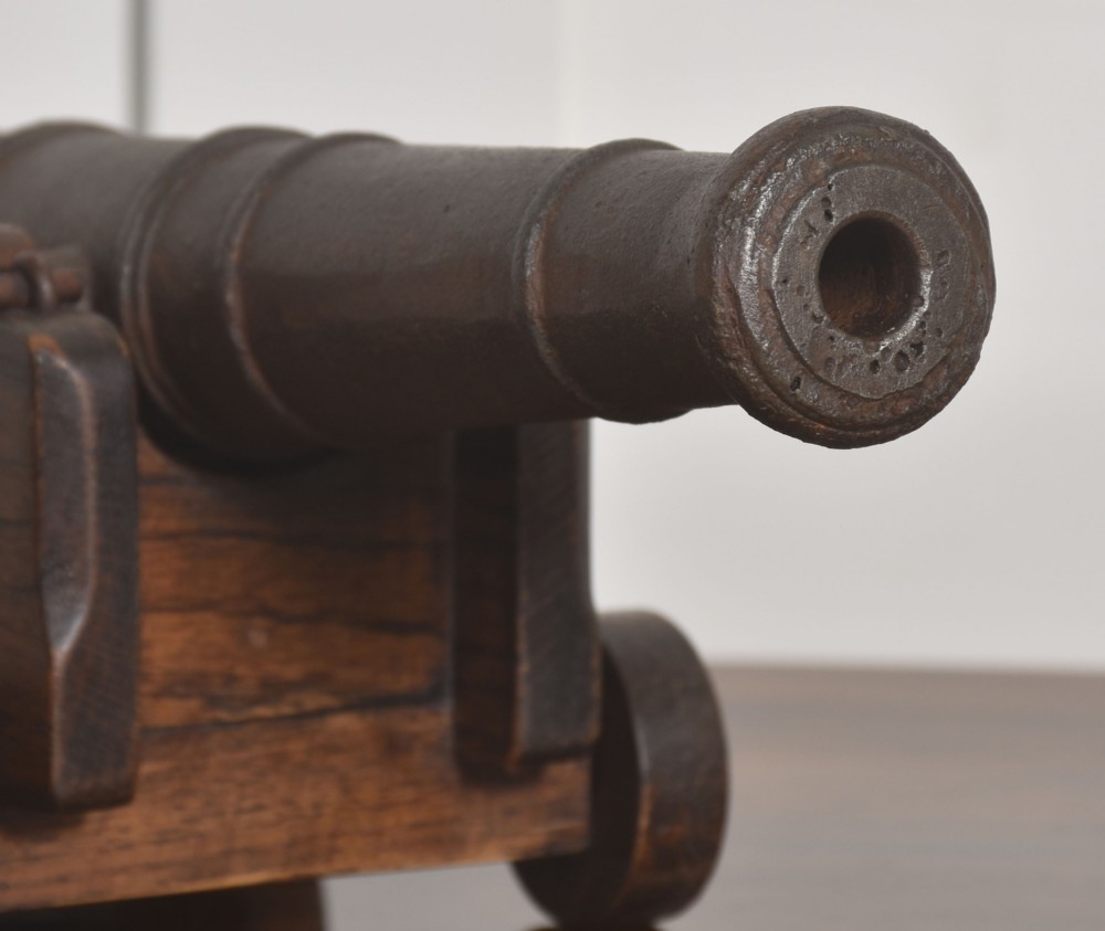 A miniature cast-iron signal cannon barrel mounted on a dark stepped oak wooden carriage with four wooden wheels. View III