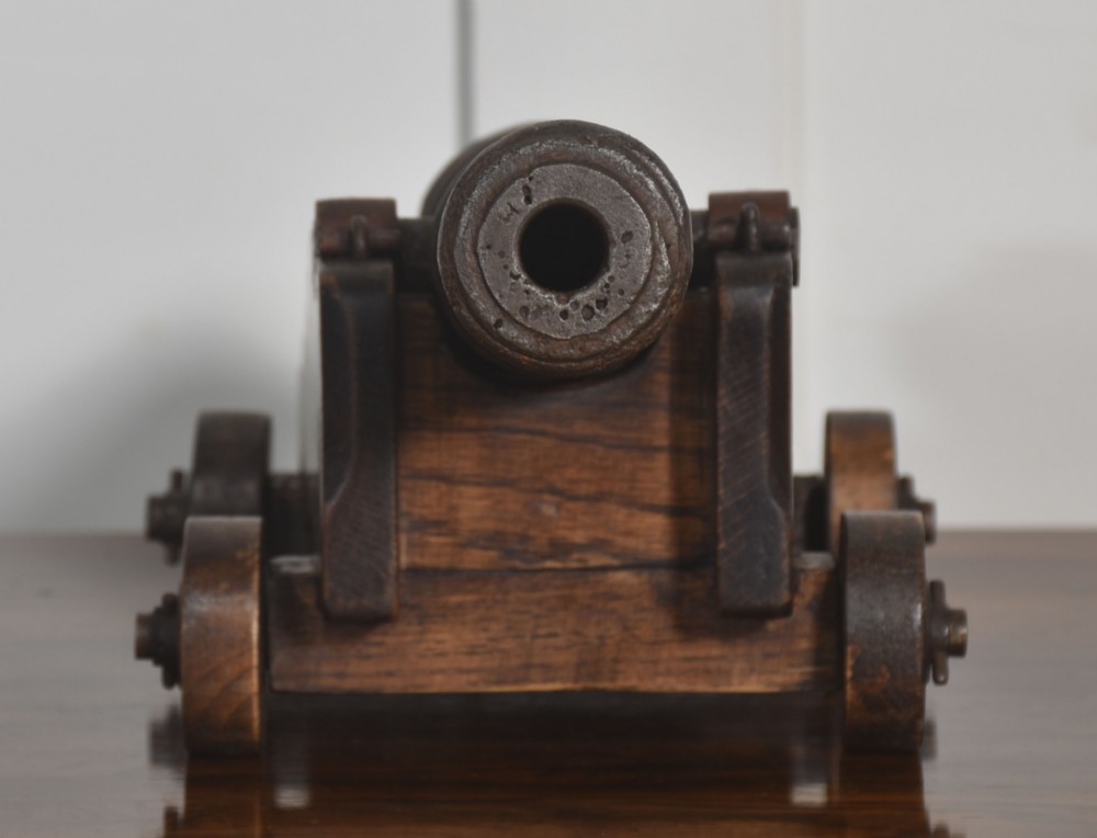A miniature cast-iron signal cannon barrel mounted on a dark stepped oak wooden carriage with four wooden wheels. View IV