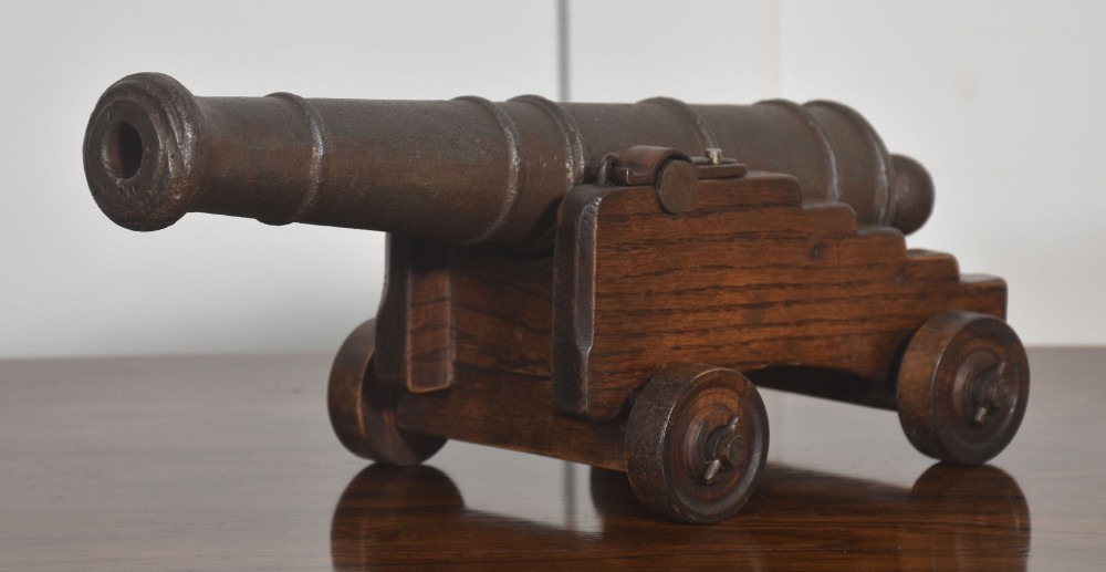 A miniature cast-iron signal cannon barrel mounted on a dark stepped oak wooden carriage with four wooden wheels. View V