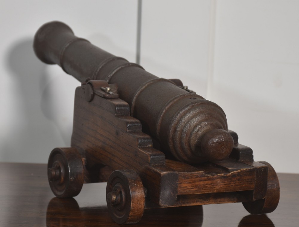 A miniature cast-iron signal cannon barrel mounted on a dark stepped oak wooden carriage with four wooden wheels. View VI