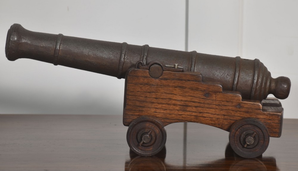 A miniature cast-iron signal cannon barrel mounted on a dark stepped oak wooden carriage with four wooden wheels. View VII