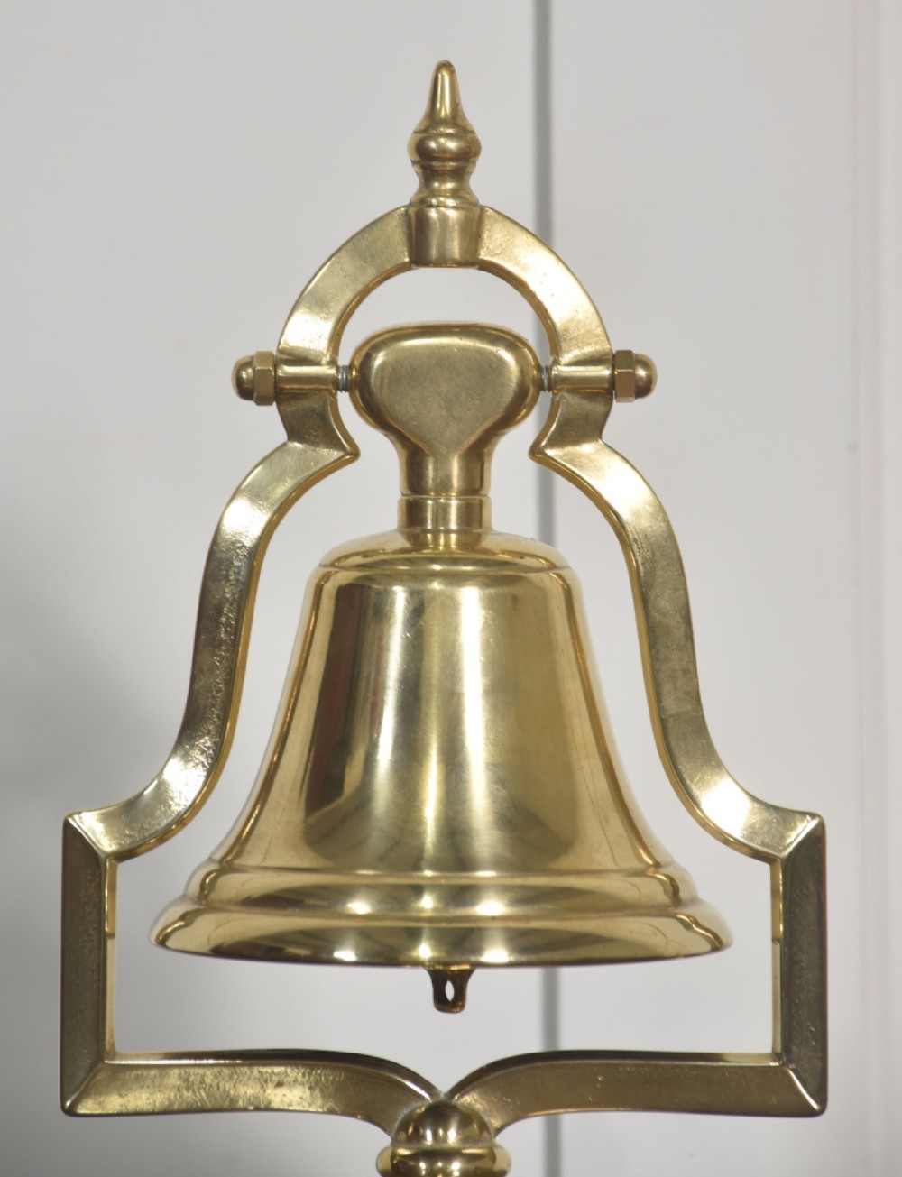 A polished brass table bell suspended within a shaped gantry frame on a tiered brass pedestal base. View III