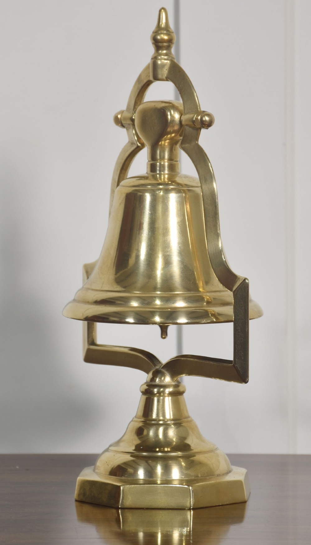 A polished brass table bell suspended within a shaped gantry frame on a tiered brass pedestal base. View IV