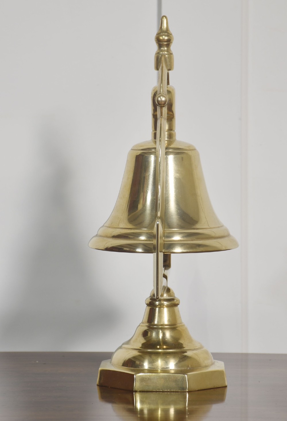 A polished brass table bell suspended within a shaped gantry frame on a tiered brass pedestal base. View V