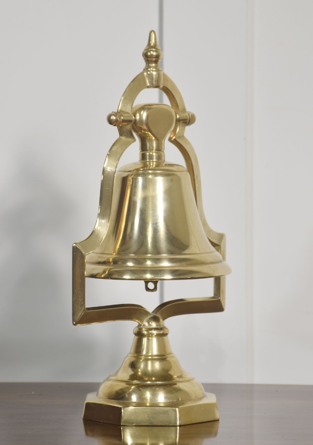A polished brass table bell suspended within a shaped gantry frame on a tiered brass pedestal base. View VI