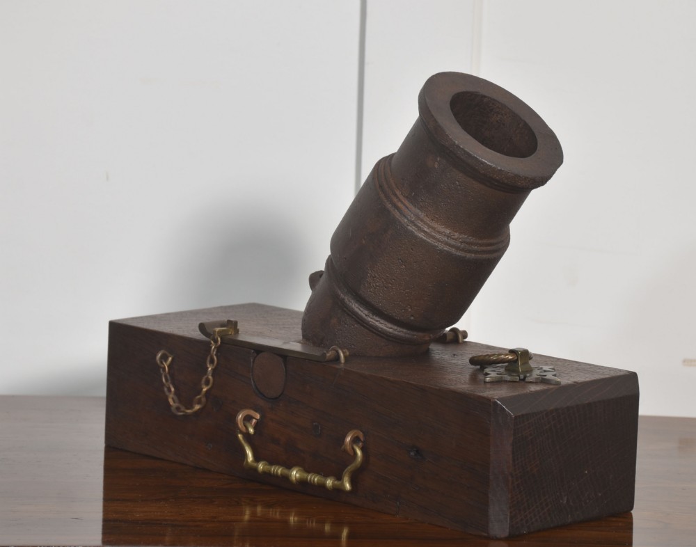 A 19th-century cast-iron signal mortar mounted at an angle on a dark oak carriage with brass side handles and chains.