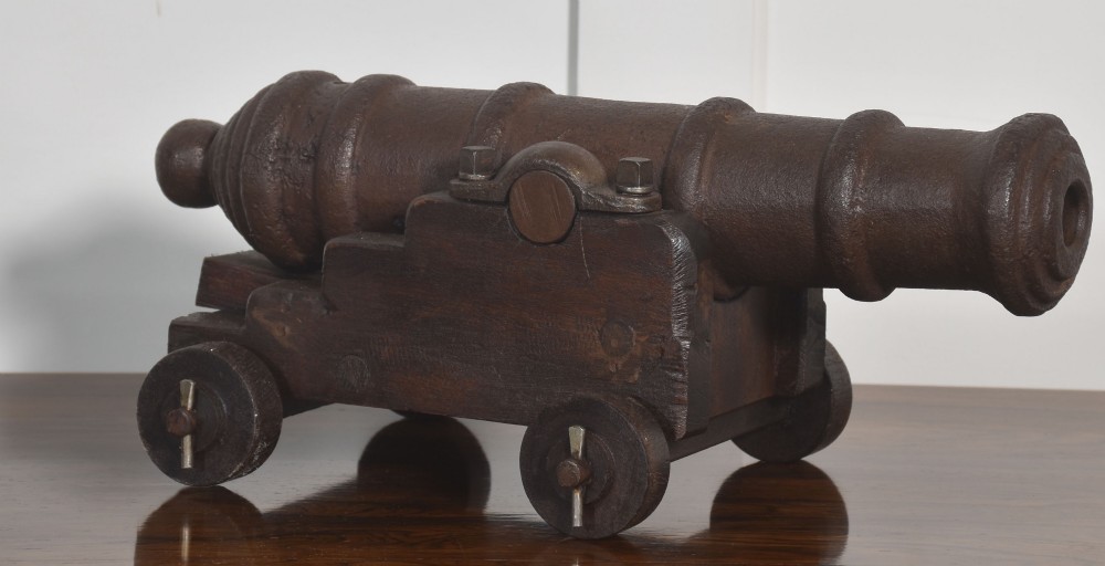 A nineteenth-century cast-iron signal cannon with a dark patina, mounted on a stepped dark oak carriage with wooden wheels. View III