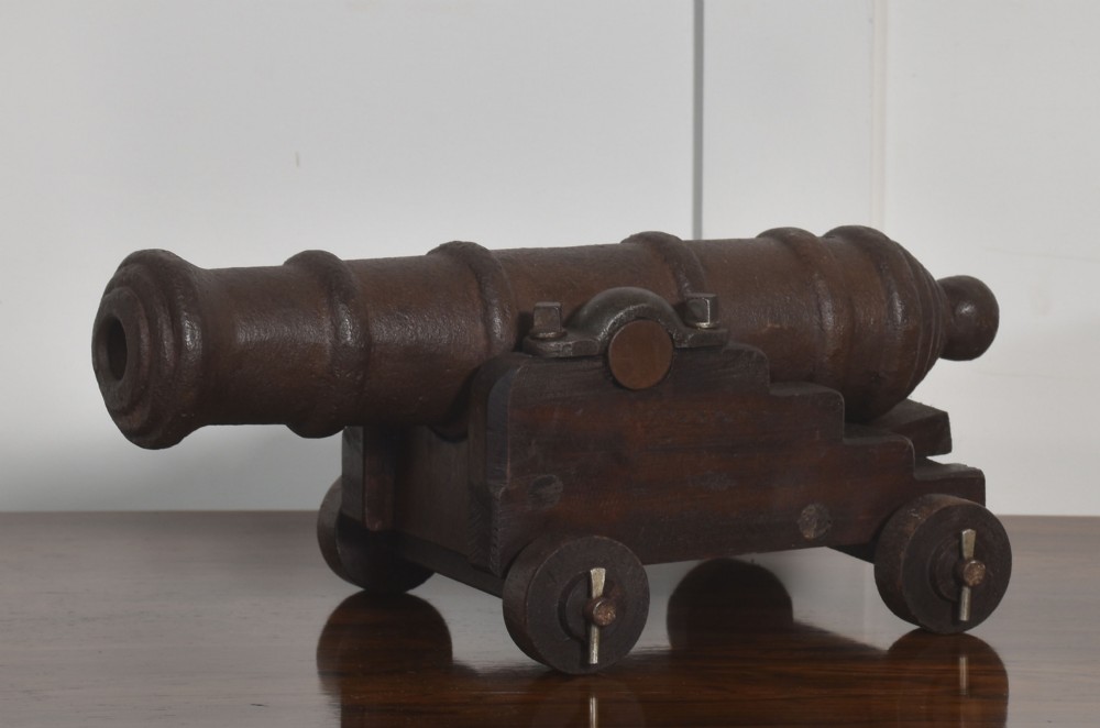 A nineteenth-century cast-iron signal cannon with a dark patina, mounted on a stepped dark oak carriage with wooden wheels. View VII