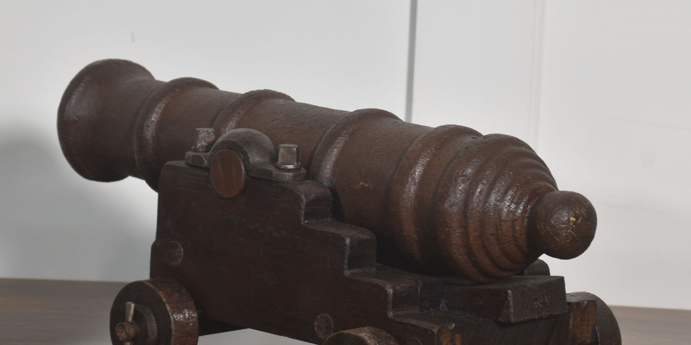 A nineteenth-century cast-iron signal cannon with a dark patina, mounted on a stepped dark oak carriage with wooden wheels. View VIII