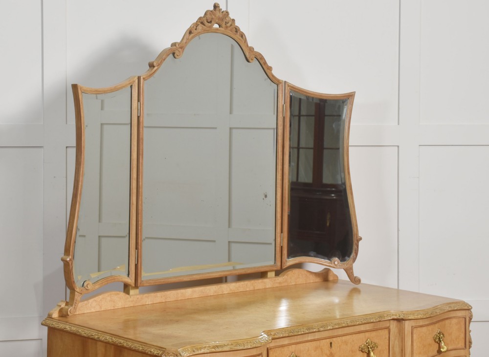 A light burr walnut dressing table featuring five drawers, brass handles, carved cabriole legs, a three-piece folding mirror, and a matching upholstered stool. View V