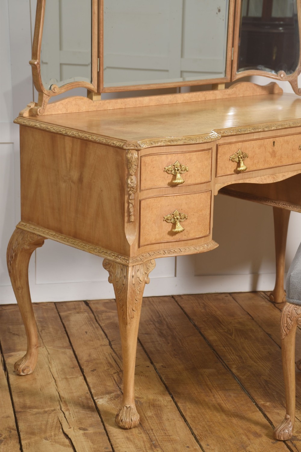 A light burr walnut dressing table featuring five drawers, brass handles, carved cabriole legs, a three-piece folding mirror, and a matching upholstered stool. View VII
