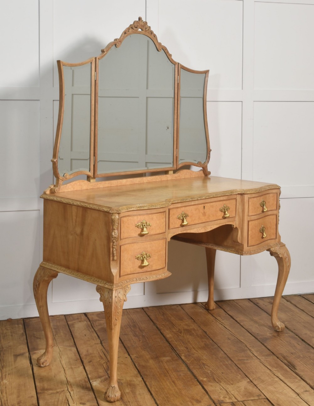 A light burr walnut dressing table featuring five drawers, brass handles, carved cabriole legs, a three-piece folding mirror, and a matching upholstered stool. View VIII