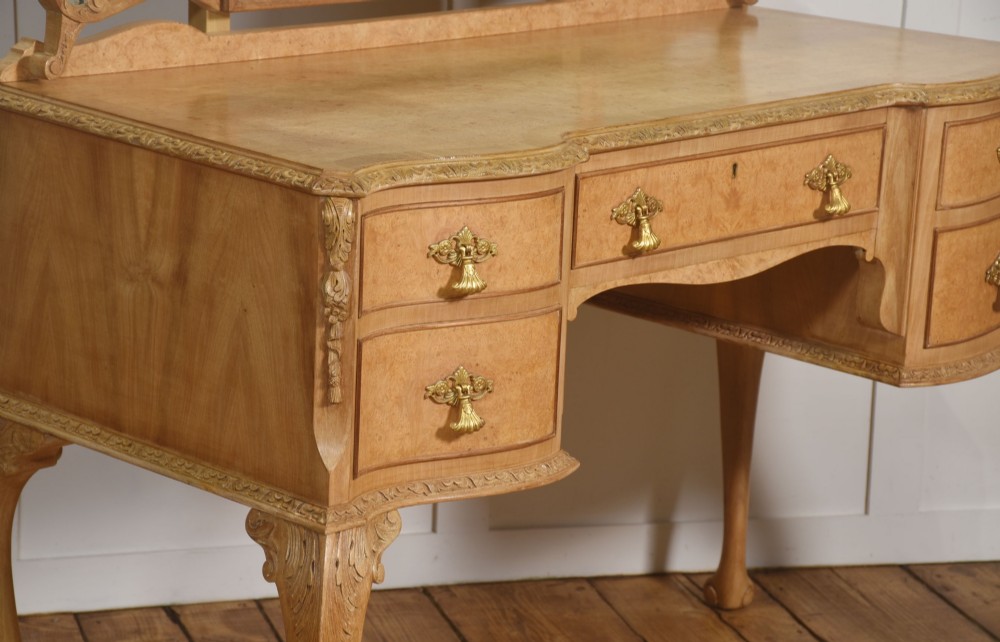 A light burr walnut dressing table featuring five drawers, brass handles, carved cabriole legs, a three-piece folding mirror, and a matching upholstered stool. View IX