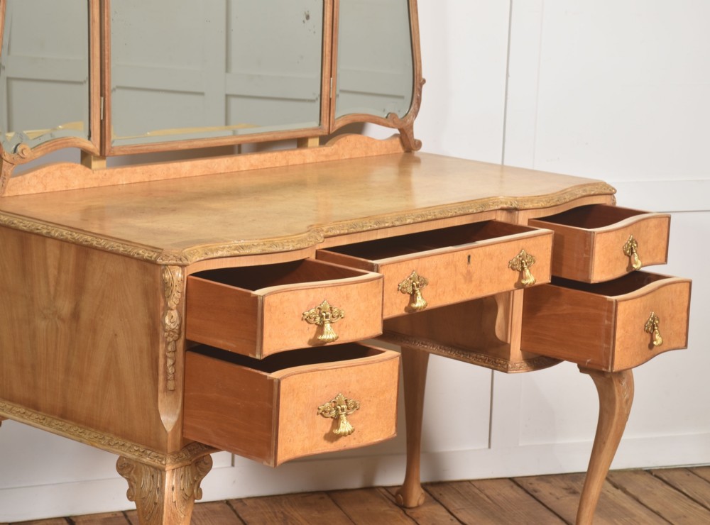 A light burr walnut dressing table featuring five drawers, brass handles, carved cabriole legs, a three-piece folding mirror, and a matching upholstered stool. View XI