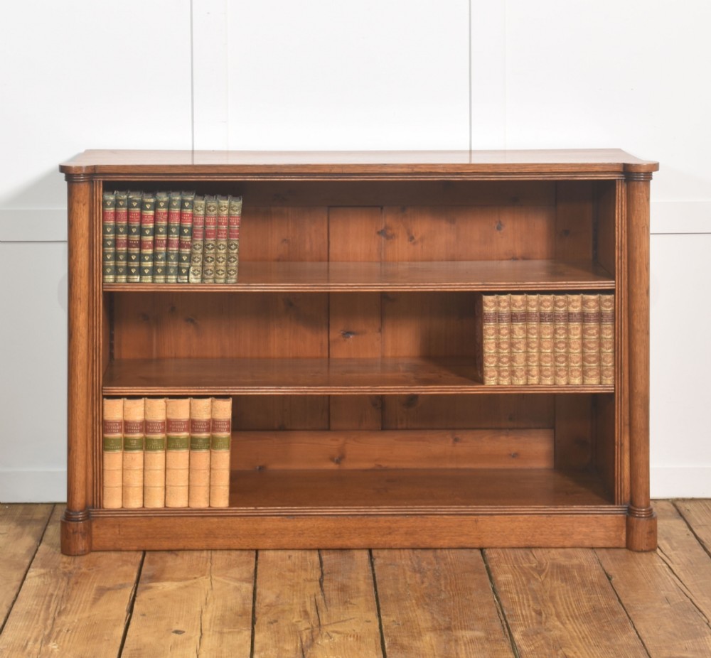 A late nineteenth-century warm brown oak open bookcase featuring three horizontal shelves flanked by fluted side pilasters on a plinth base.