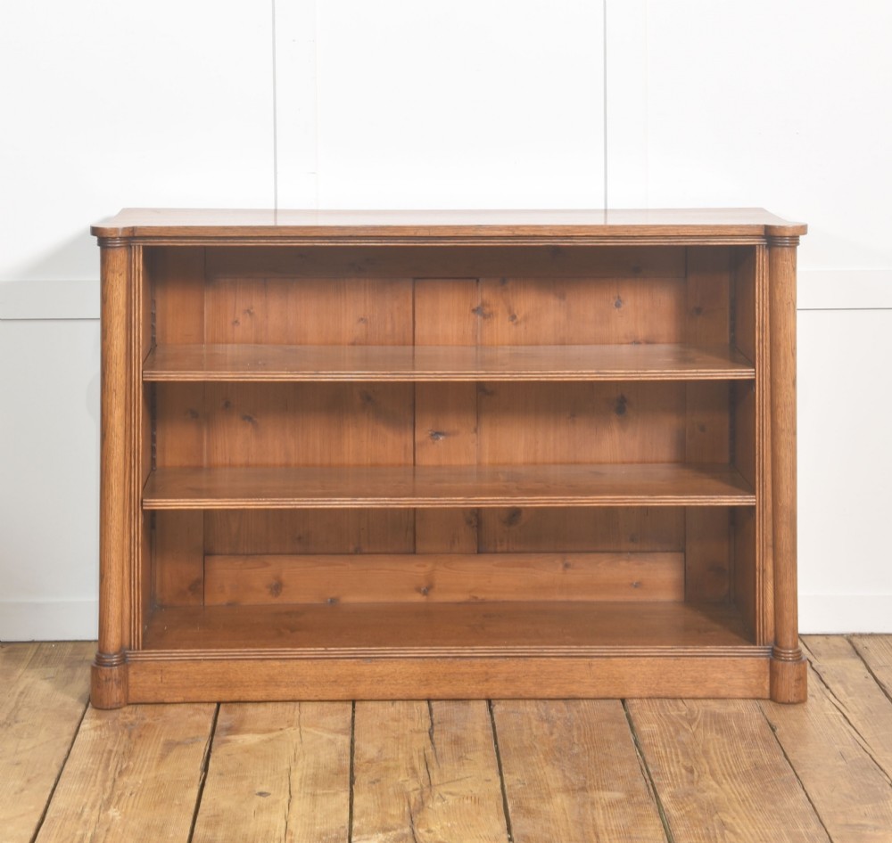 A late nineteenth-century warm brown oak open bookcase featuring three horizontal shelves flanked by fluted side pilasters on a plinth base. View IX