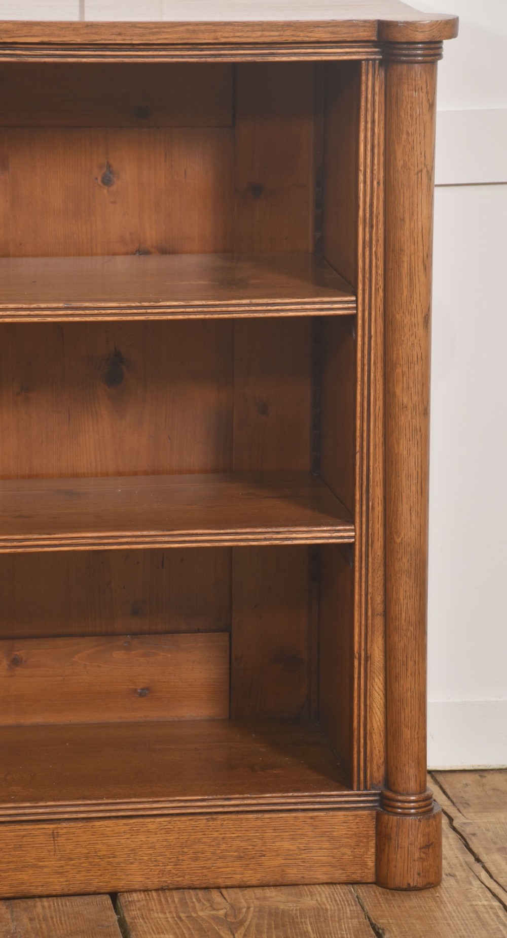 A late nineteenth-century warm brown oak open bookcase featuring three horizontal shelves flanked by fluted side pilasters on a plinth base. View X