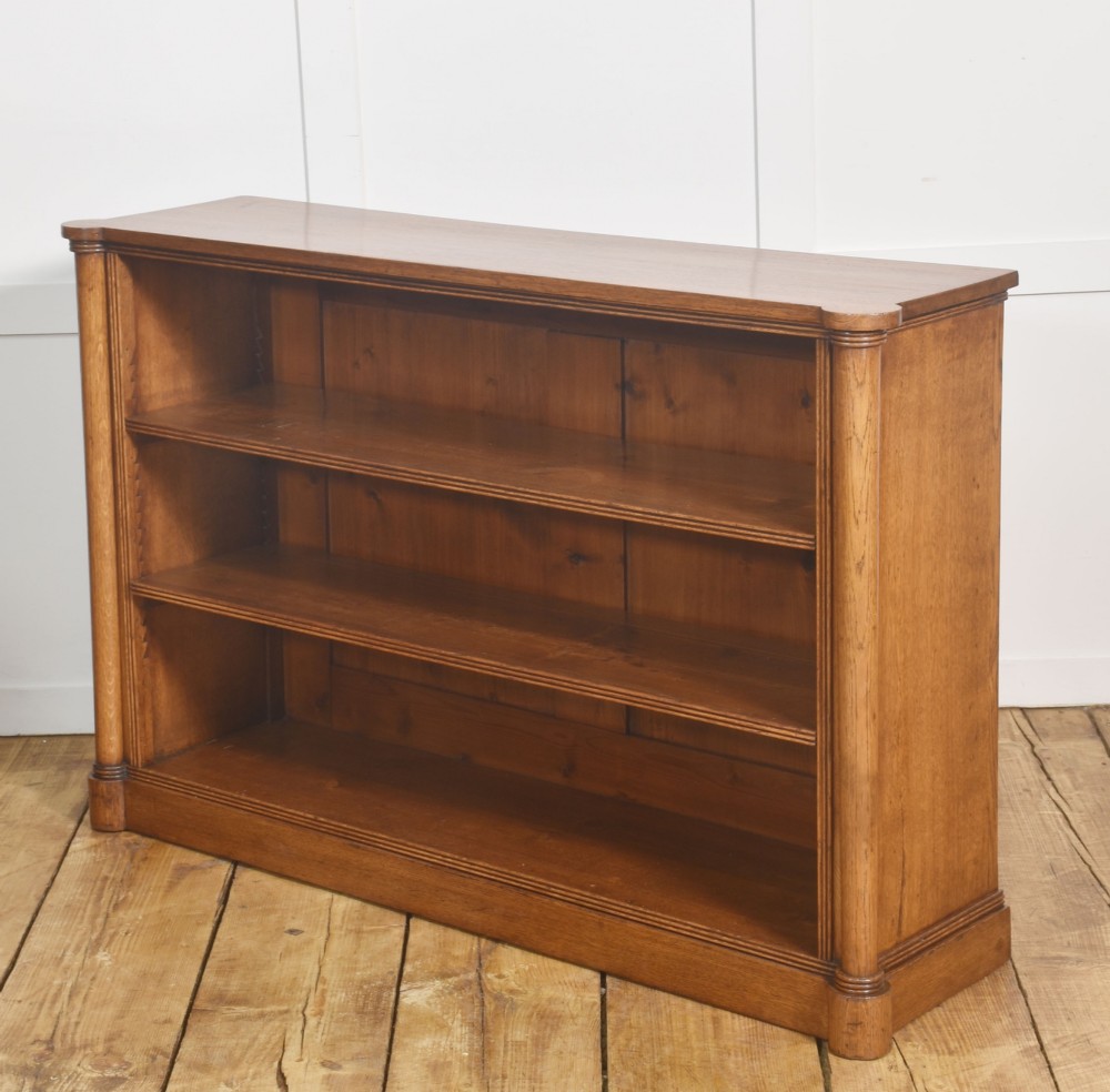 A late nineteenth-century warm brown oak open bookcase featuring three horizontal shelves flanked by fluted side pilasters on a plinth base. View XII