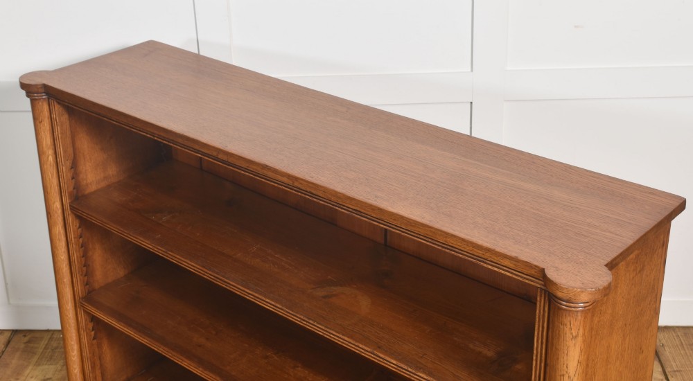 A late nineteenth-century warm brown oak open bookcase featuring three horizontal shelves flanked by fluted side pilasters on a plinth base. View XIII