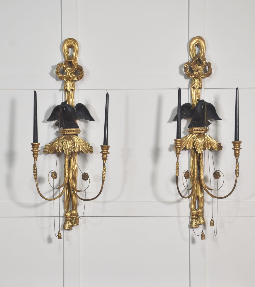 A pair of George III style giltwood wall sconces featuring carved ribbon crestings, dark eagle motifs, and twin candle arms. View II