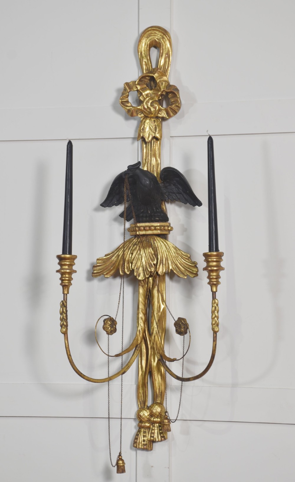 A pair of George III style giltwood wall sconces featuring carved ribbon crestings, dark eagle motifs, and twin candle arms. View V