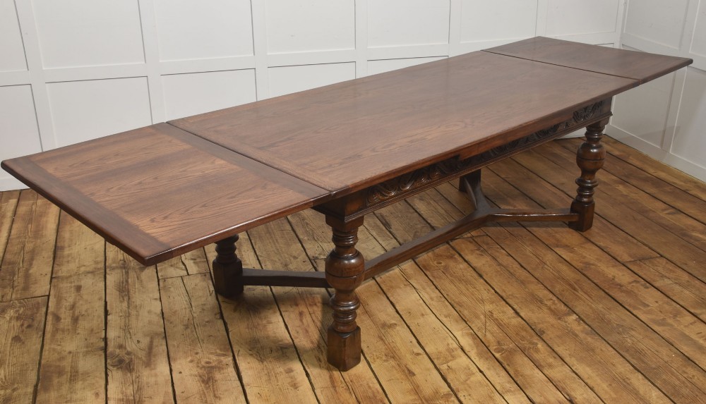 An extended dark oak Jacobean style dining table featuring carved friezes, turned baluster legs, and a sturdy stretcher base.