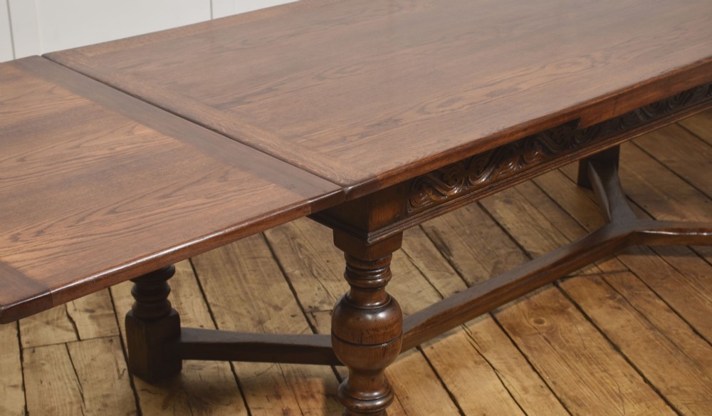 An extended dark oak Jacobean style dining table featuring carved friezes, turned baluster legs, and a sturdy stretcher base. View III