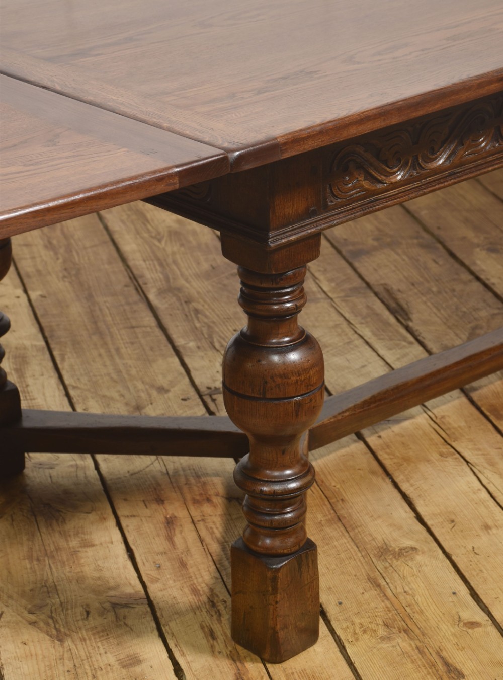 An extended dark oak Jacobean style dining table featuring carved friezes, turned baluster legs, and a sturdy stretcher base. View IV