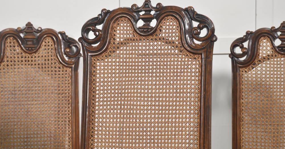 A set of eight walnut dining chairs featuring tall carved frames, woven cane back panels, grey upholstered seats, and scrollwork stretchers. View IV