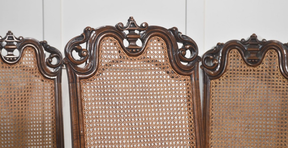 A set of eight walnut dining chairs featuring tall carved frames, woven cane back panels, grey upholstered seats, and scrollwork stretchers. View V