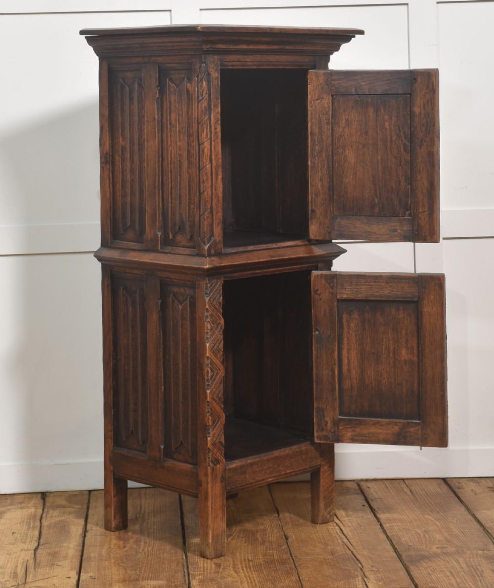 A tall, narrow dark oak Gothic Revival cabinet with two carved cupboard doors, decorative iron strap hinges, and a moulded top cornice. View V