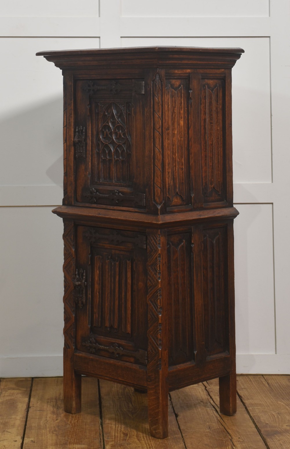 A tall, narrow dark oak Gothic Revival cabinet with two carved cupboard doors, decorative iron strap hinges, and a moulded top cornice. View VI