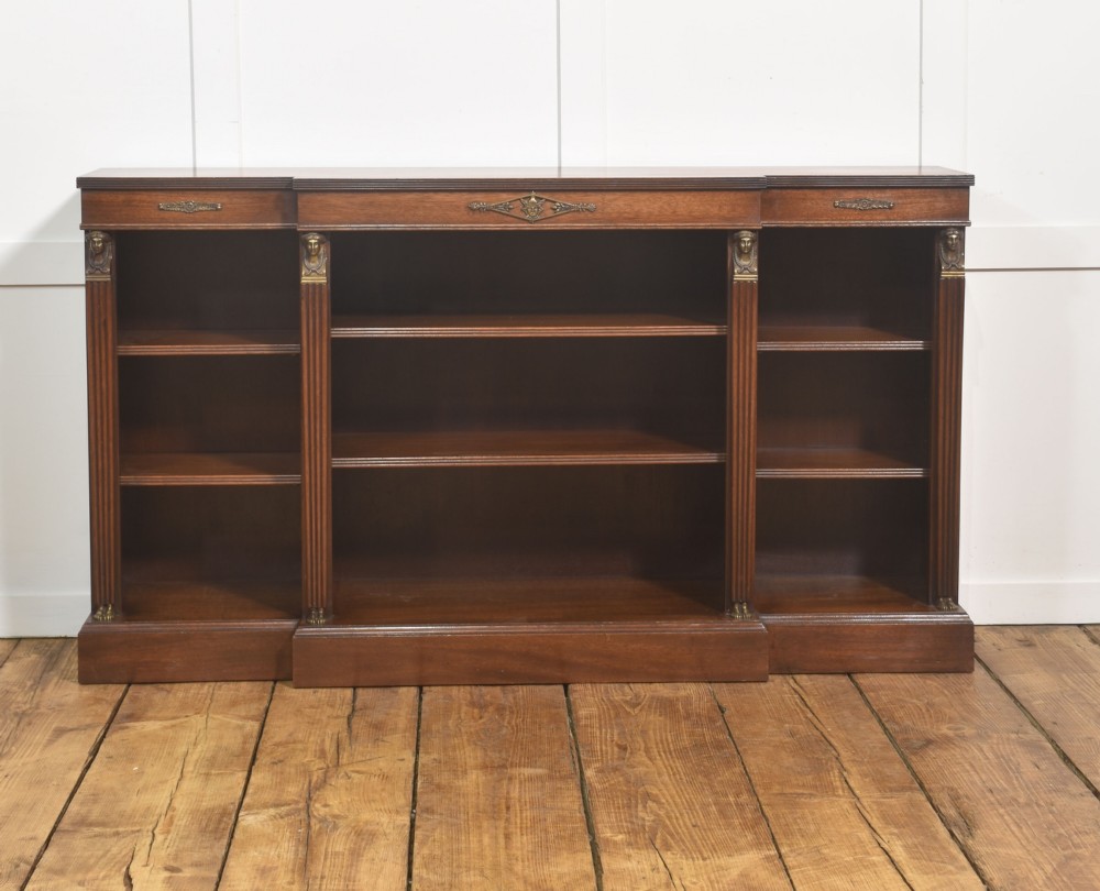 A low Regency style mahogany breakfront open bookcase featuring fluted pilasters, brass mounts, and adjustable shelves.