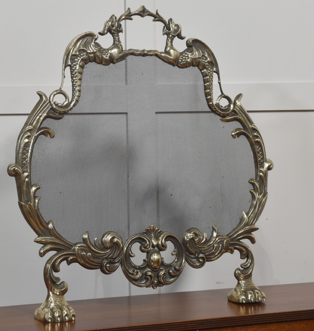An ornate brass Rococo Revival fire screen featuring a central wire mesh panel, dragon-shaped top handles, and detailed claw feet. View III