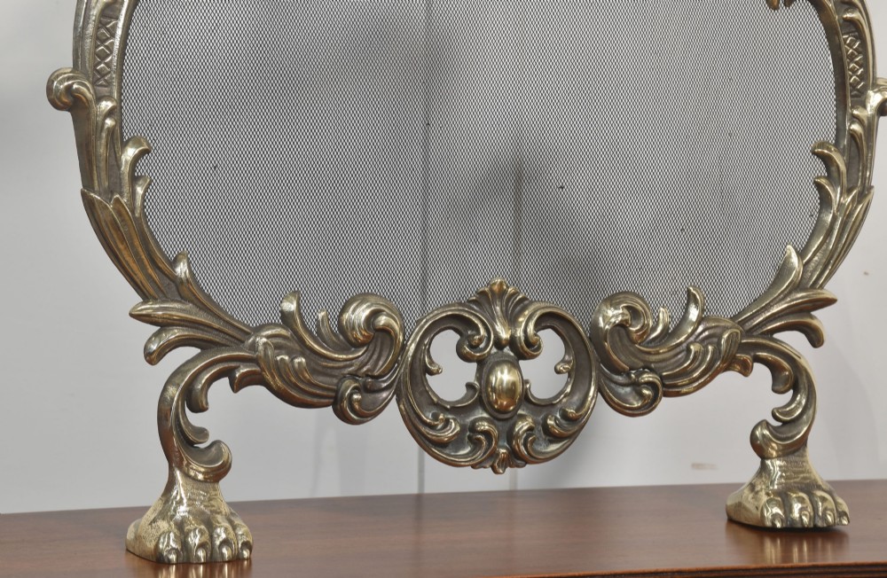 An ornate brass Rococo Revival fire screen featuring a central wire mesh panel, dragon-shaped top handles, and detailed claw feet. View IV