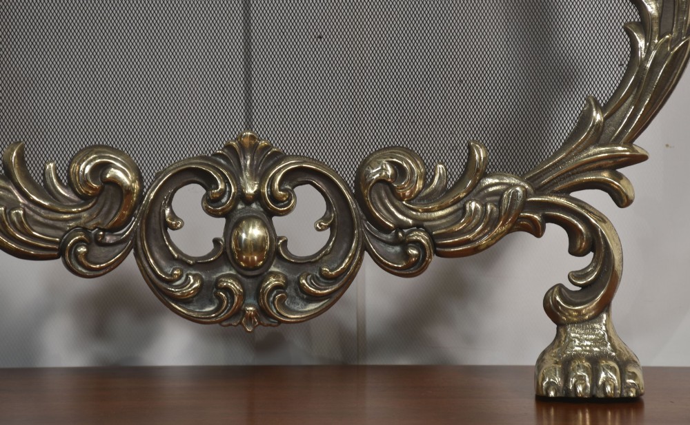 An ornate brass Rococo Revival fire screen featuring a central wire mesh panel, dragon-shaped top handles, and detailed claw feet. View VII