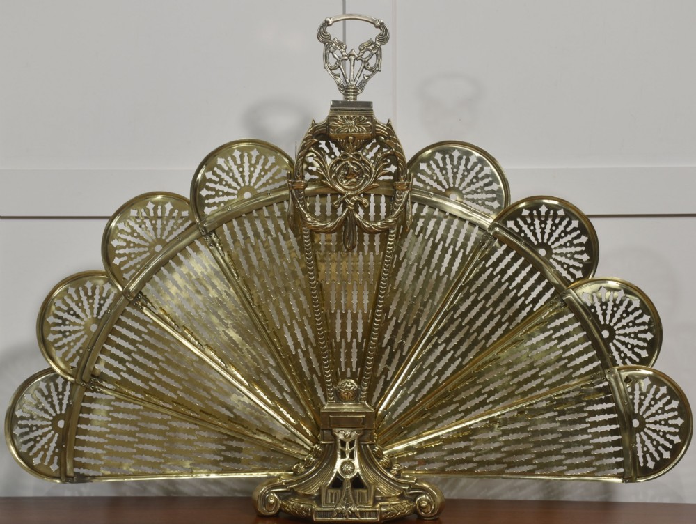 A Victorian brass peacock fire screen with pierced filigree fan blades expanding from a cast metal pedestal base. View VII