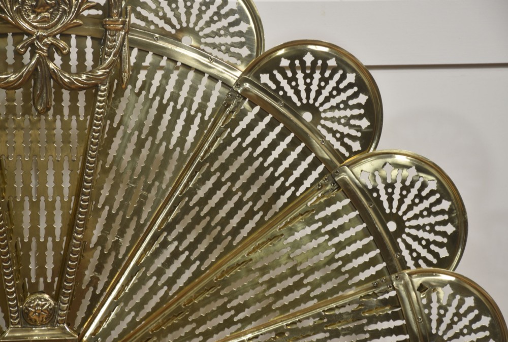 A Victorian brass peacock fire screen with pierced filigree fan blades expanding from a cast metal pedestal base. View VIII