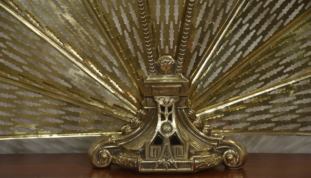 A Victorian brass peacock fire screen with pierced filigree fan blades expanding from a cast metal pedestal base. View IX