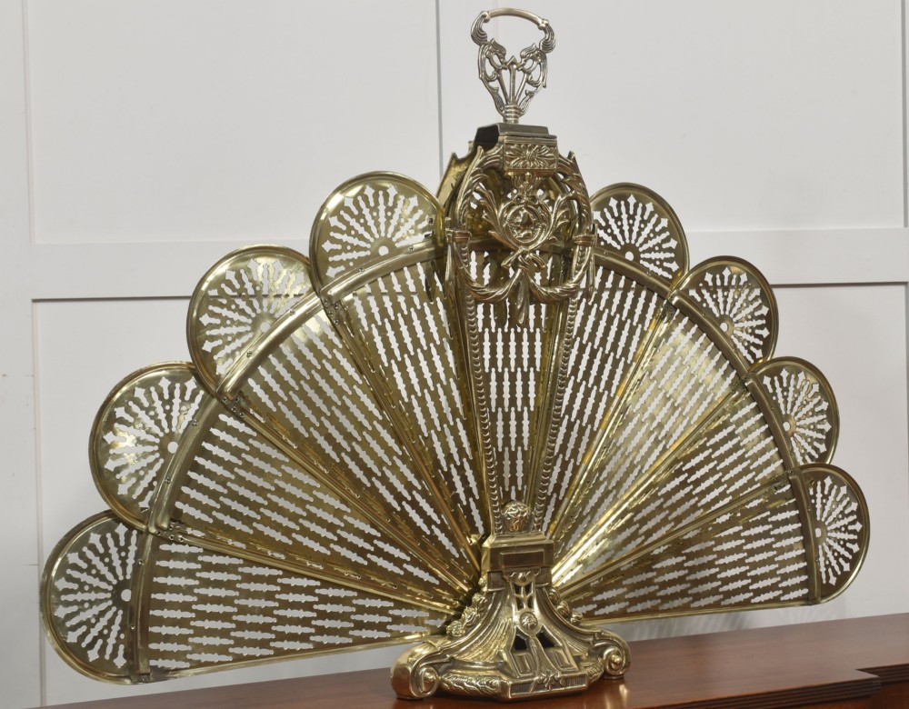 A Victorian brass peacock fire screen with pierced filigree fan blades expanding from a cast metal pedestal base. View X