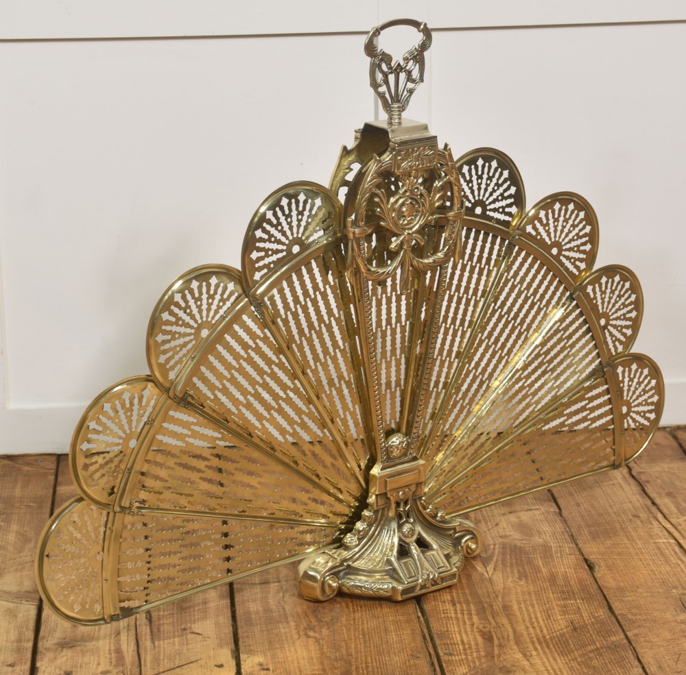 A Victorian brass peacock fire screen with pierced filigree fan blades expanding from a cast metal pedestal base.