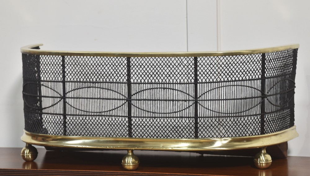 A curved antique fire guard made from black woven wirework with a polished brass top rim, base trim, and turned ball feet. View VIII